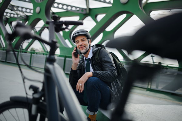 A businessman with bike sitting on bench, using smartphone. Commuting and alternative transport concept