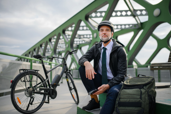 A businessman with bike sitting on bench, using smartphone. Commuting and alternative transport concept