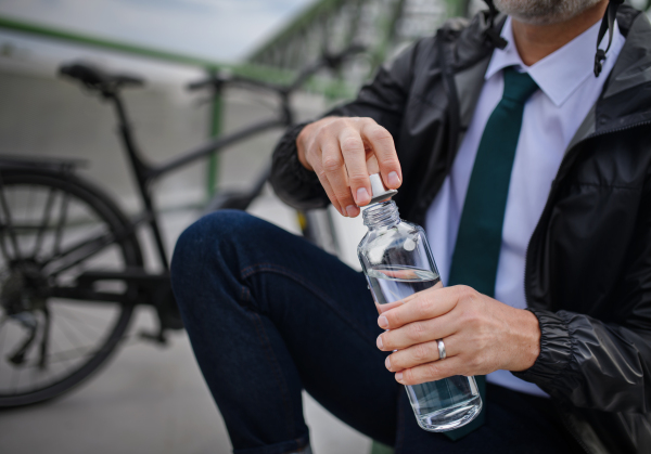 Portrait of businessman resting in a bench next to his bike, drinking water, sustainable lifestyle concept.