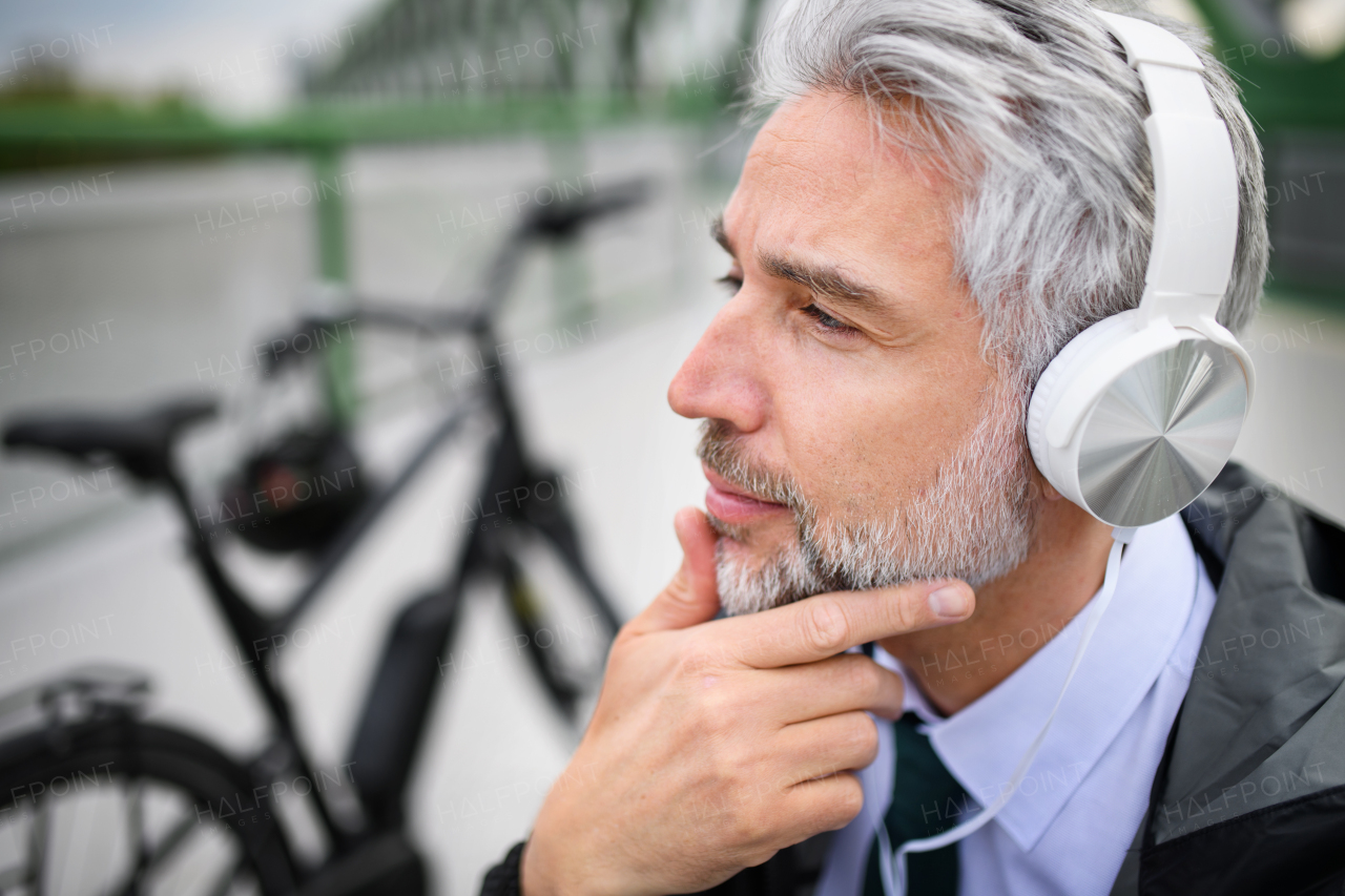 A businessman with bike sitting on bench, listening to music and resting. Commuting and alternative transport concept