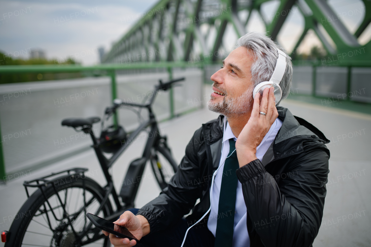 A businessman with bike sitting on bench, listening to music and resting. Commuting and alternative transport concept