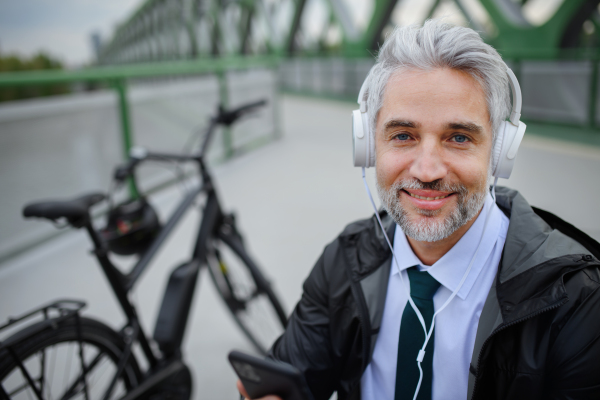 A businessman with bike sitting on bench, listening to music with feet up and resting. Commuting and alternative transport concept