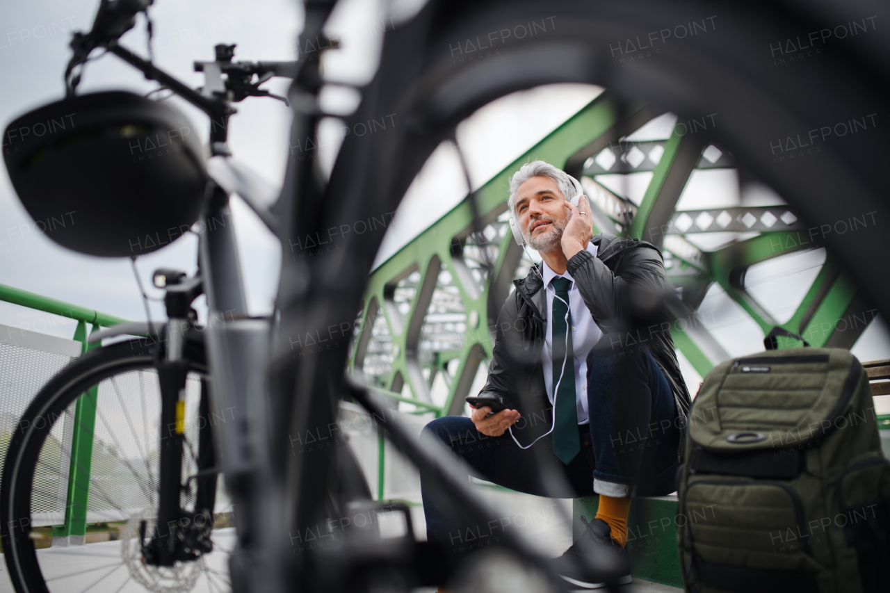 A businessman with bike sitting on bench, using smartphone. Commuting and alternative transport concept