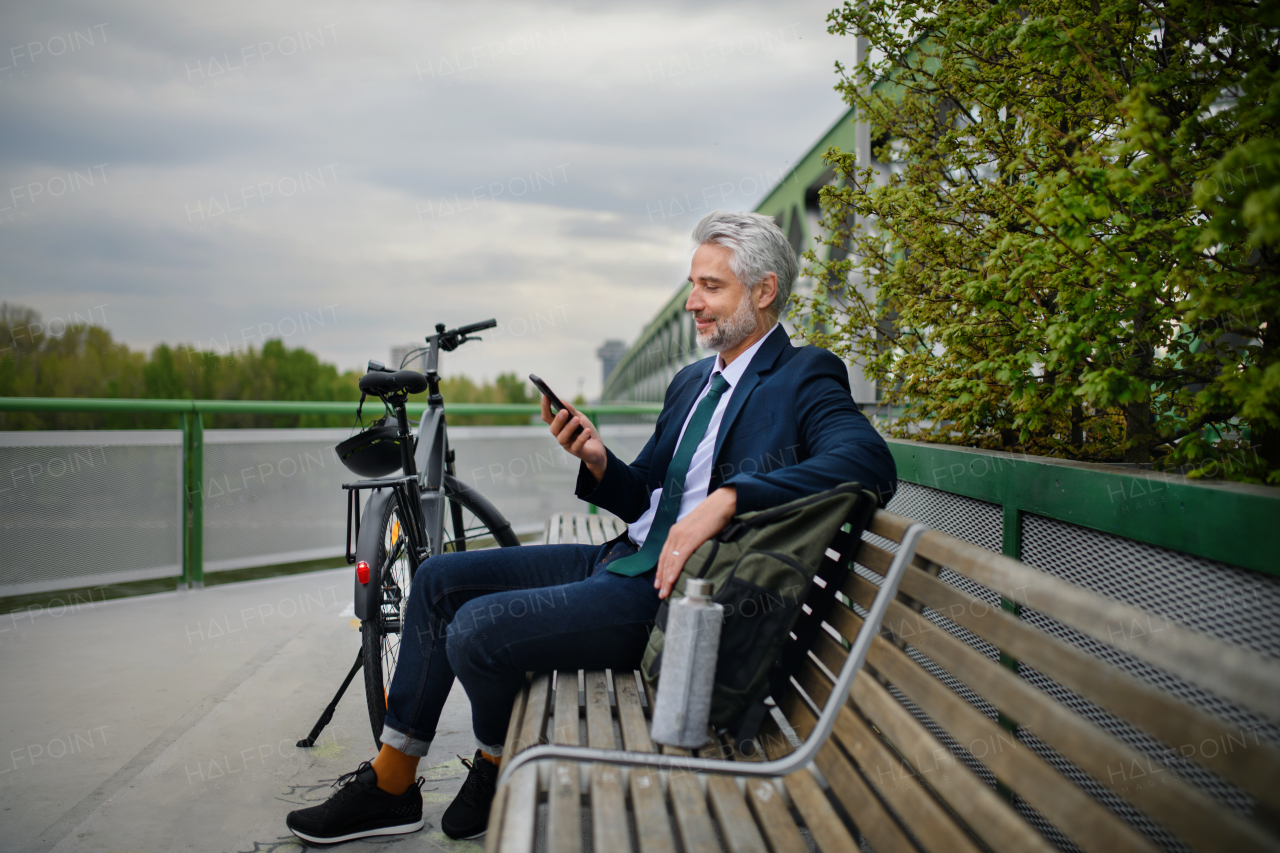 A businessman with bike sitting on bench, listening to music with feet up and resting. Commuting and alternative transport concept