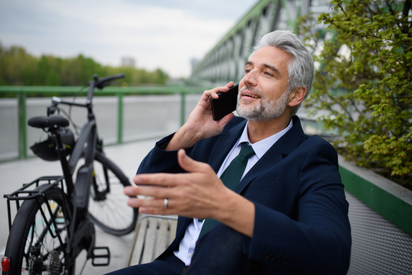 A businessman with bike sitting on bench, using smartphone. Commuting and alternative transport concept