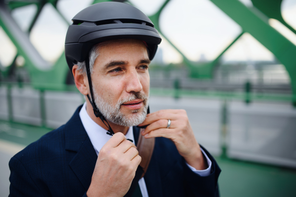 A portrait of businessman commuter on the way to work putting on cycling helmet, sustainable lifestyle concept.