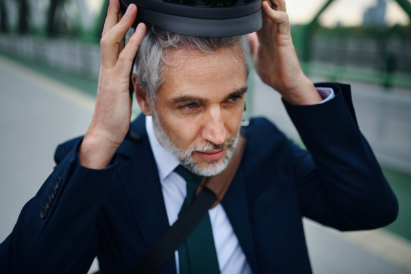 A portrait of businessman commuter on the way to work putting on cycling helmet, sustainable lifestyle concept.