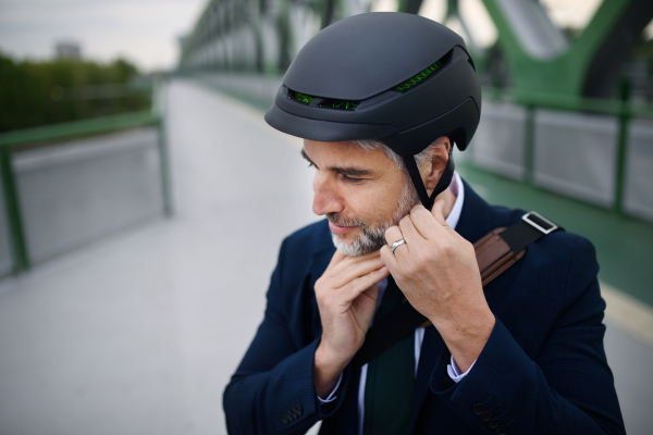 A portrait of businessman commuter on the way to work putting on cycling helmet, sustainable lifestyle concept.