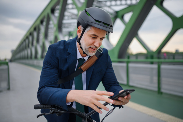 A businessman commuter on the way to work, pushing bike on bridge and texting on mobile phone, sustainable lifestyle concept.