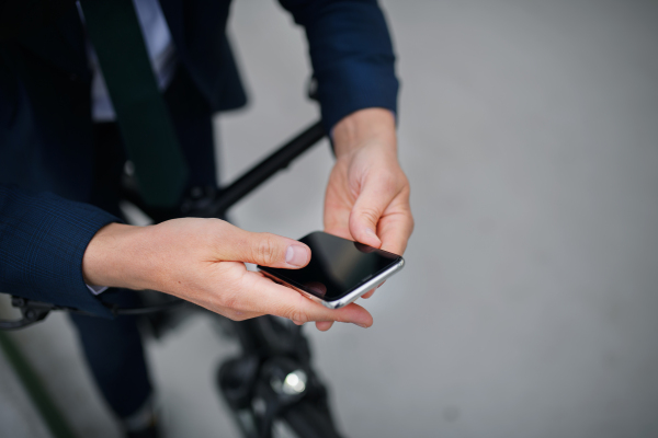 A close-up of businessman commuter on the way to work, pushing bike and using mobile phone, sustainable lifestyle concept.