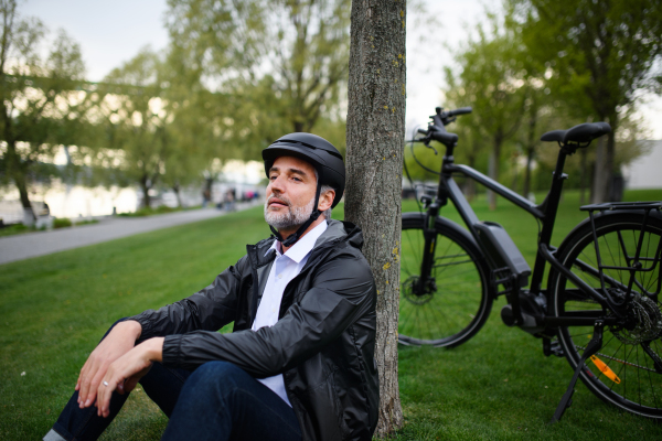 A businessman with bike sitting on grass in park, enjoying leisure time. Commuting and alternative transport concept.