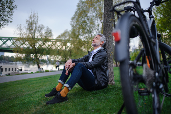 A businessman with bike sitting on grass in park, enjoying leisure time. Commuting and alternative transport concept.