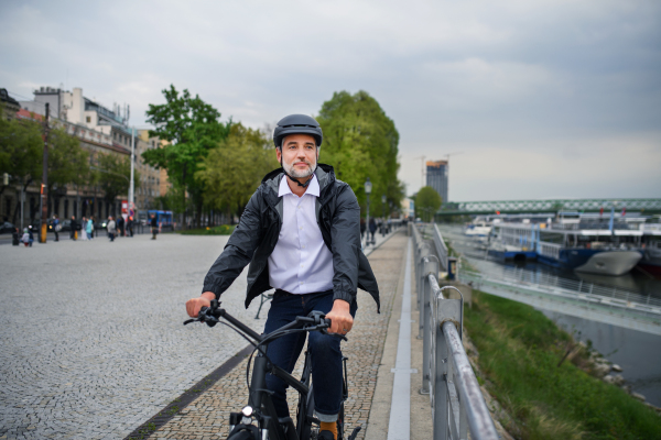 A businessman commuter on the way to work, riding bike next to river, sustainable lifestyle concept.