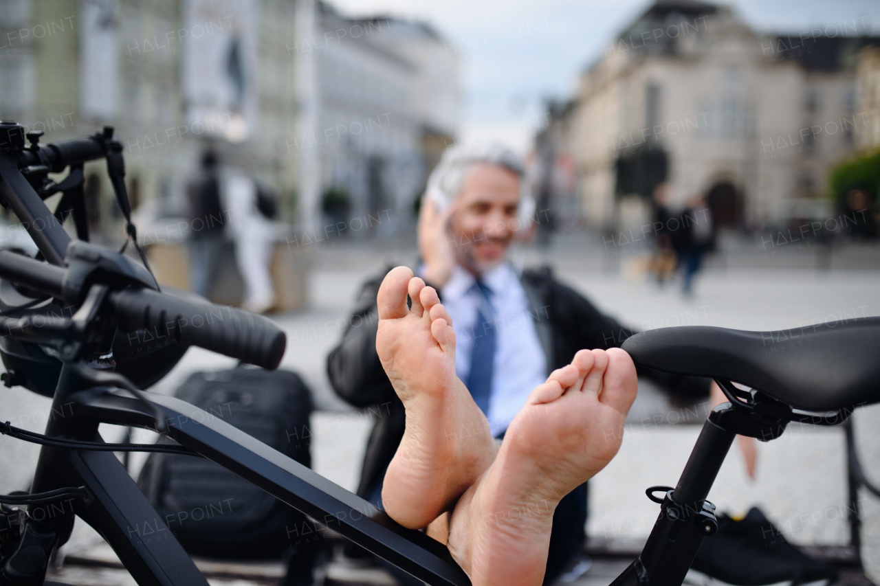 A businessman with bike sitting on bench, listening to music with feet up and resting. Commuting and alternative transport concept