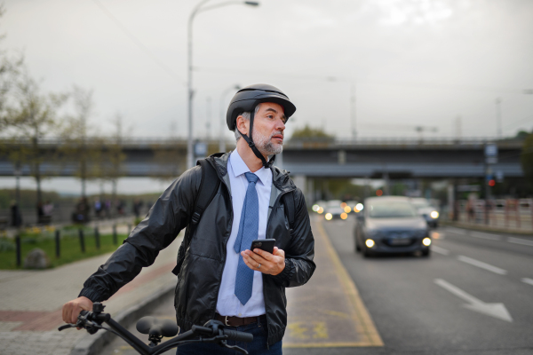 A portrait of businessman commuter on the way to work, pushing bike and using mobile phone, sustainable lifestyle concept.