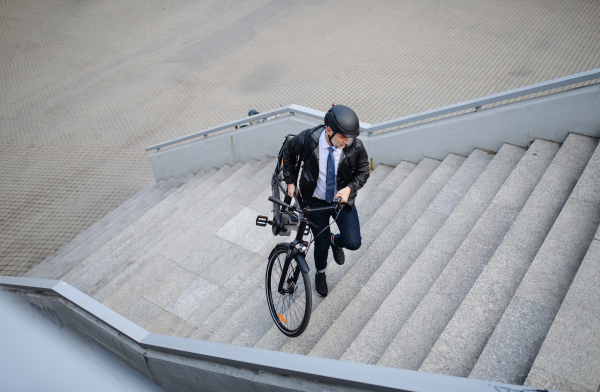 A high angle view of businessman commuter on the way to work, carrying bike upstair, sustainable lifestyle concept.