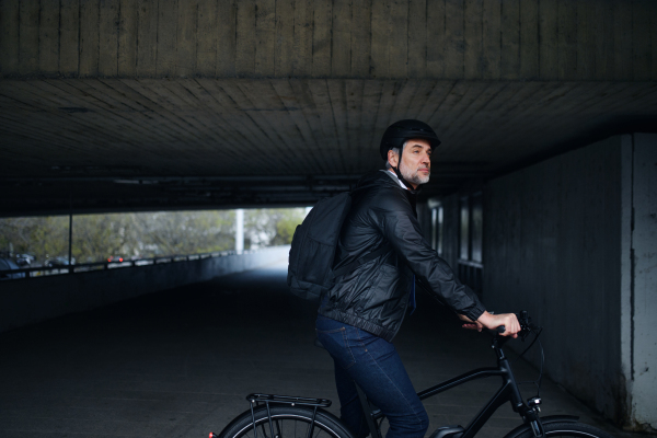 Businessman commuter on the way to work, riding bike under overpass, sustainable lifestyle concept. Copy space.