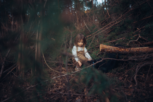 A lttle girl exploring nature outdoors in autumn forest.