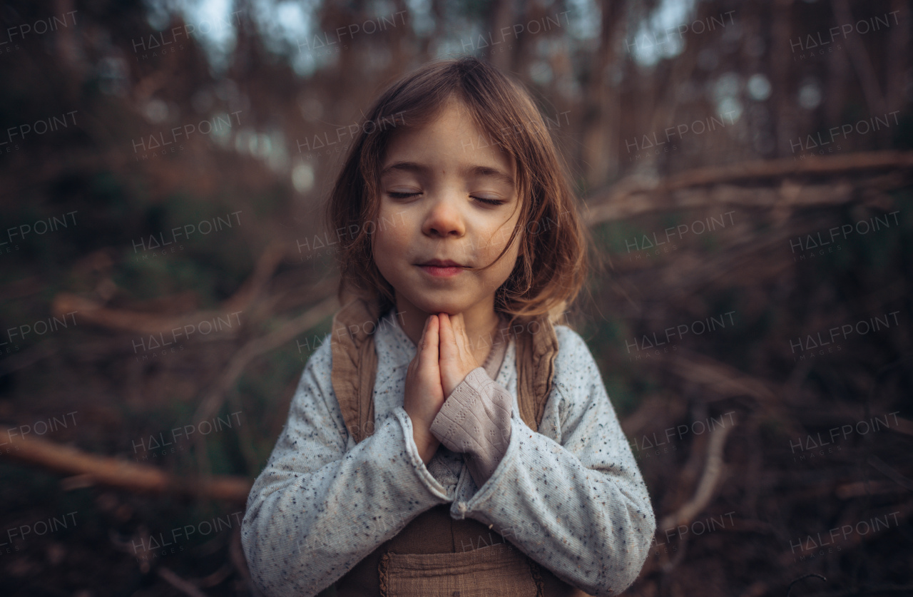 A happy little girl with closed eyes praying in autumn forest.