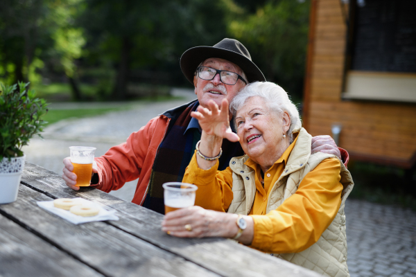 Happy senior couple in forest buffet resting after walk, having a beer and admiring nature,looking into the distance .