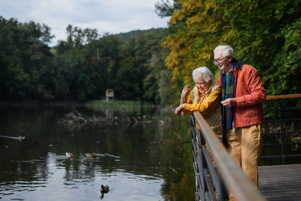 Happy senior couple at autumn walk near a lake, having break.