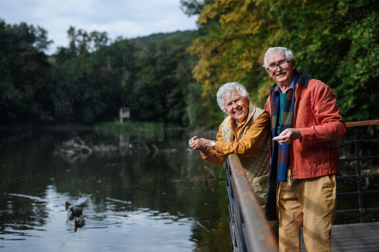 Happy senior couple at autumn walk near a lake, having break.