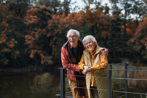 Happy senior couple at autumn walk near a lake, having break.