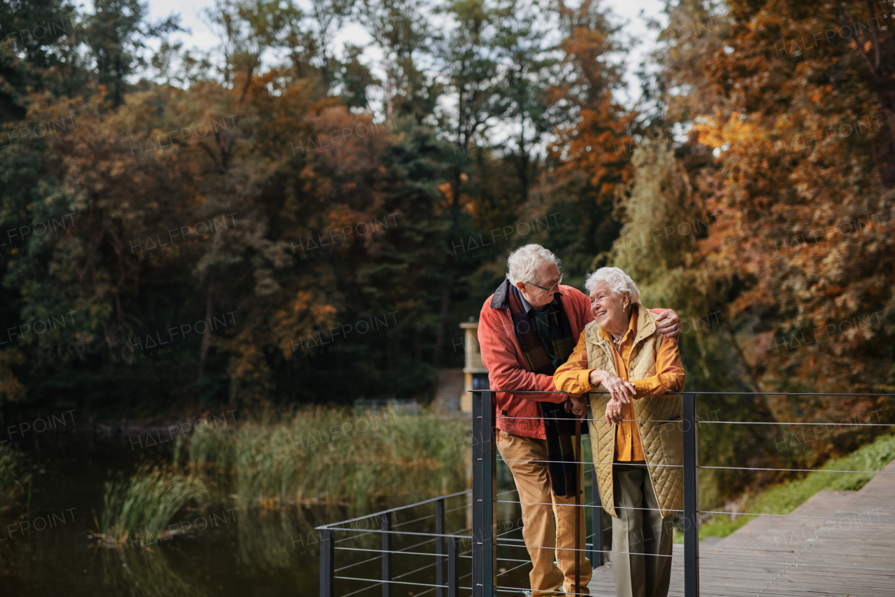 Happy senior couple at autumn walk near a lake, having break.