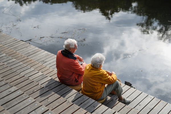 Happy senior couple at autumn walk near a lake, having break,sitting at pier.