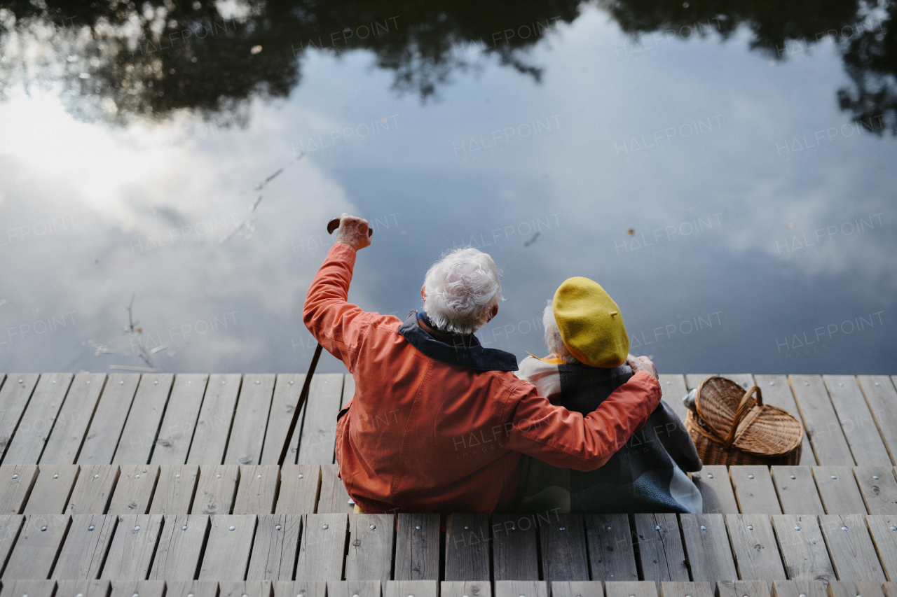 Happy senior couple at autumn walk near a lake, having break,sitting at pier.