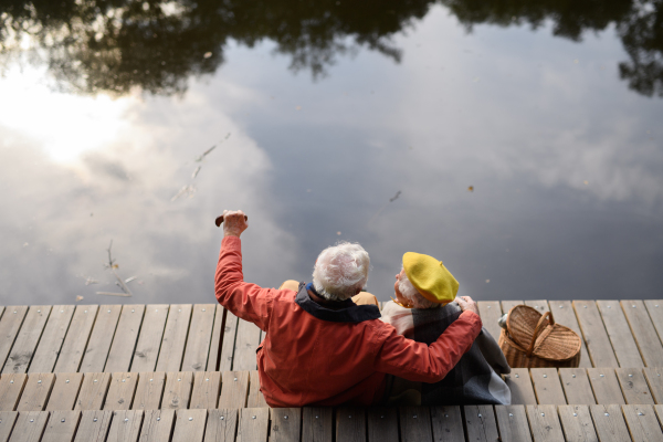 Happy senior couple at autumn walk near a lake, having break,sitting at pier.