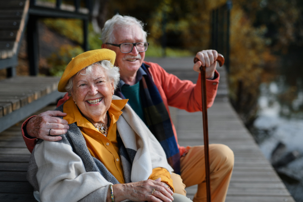 Happy senior couple in autumn clothes having break near a lake after walk.