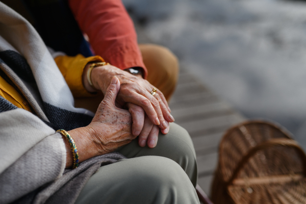 Close up of senior couple holding each other hand and sitting near a lake.