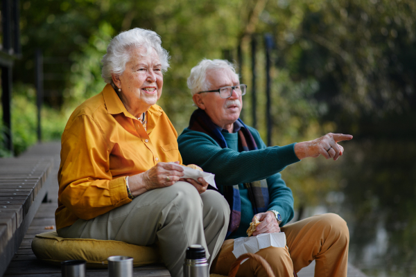 Happy senior couple resting near lake after autumn walk, looking into the distance.