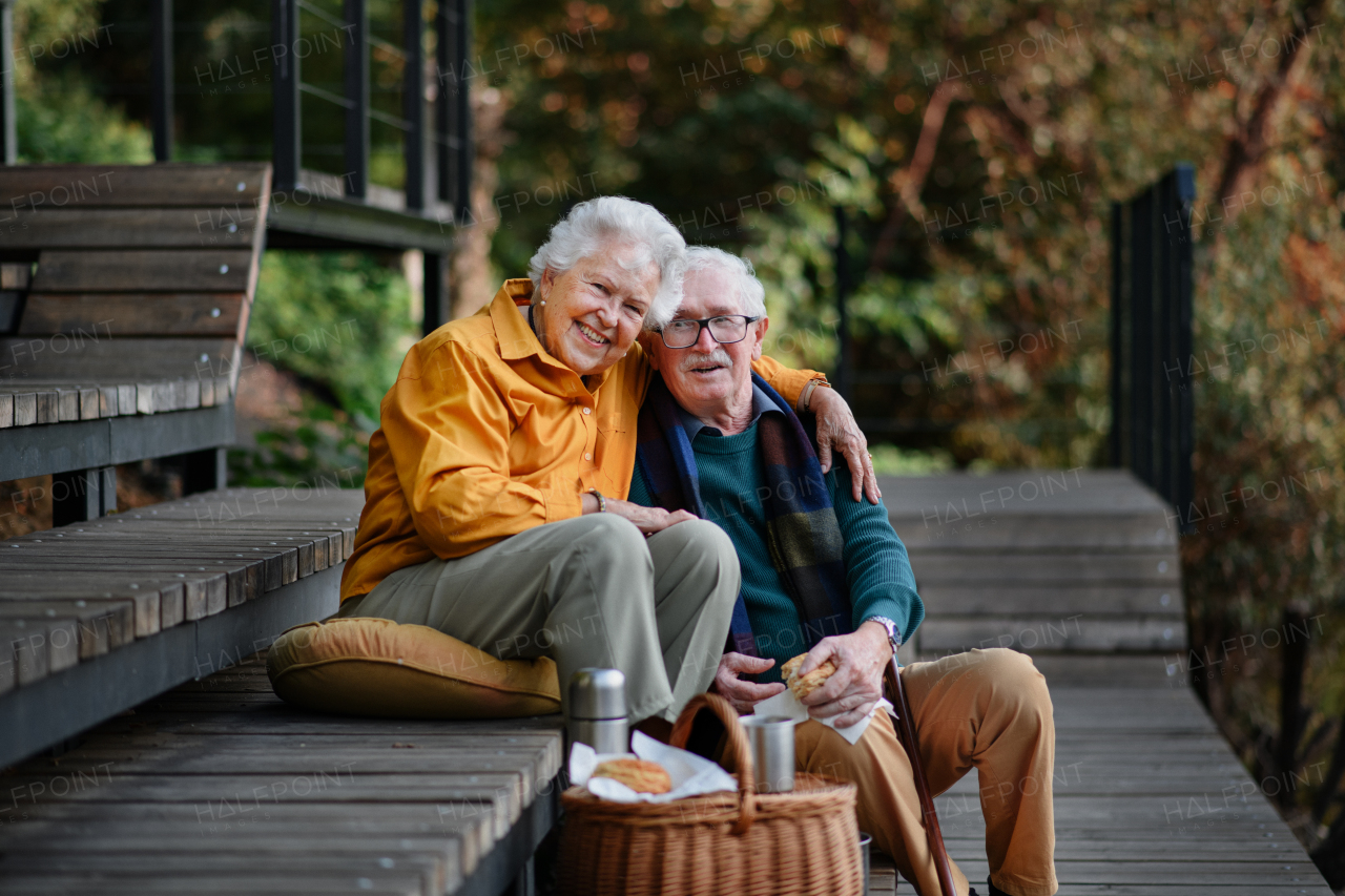 Happy senior couple resting near lake after walk and looking at a smartphone.