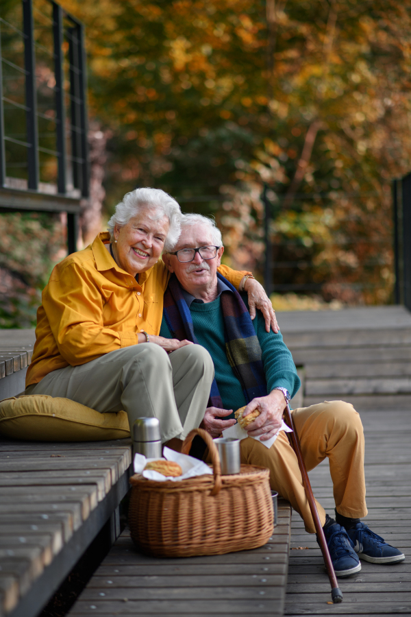 Portrait of happy senior couple having picnic and resting near lake after autumn walk.