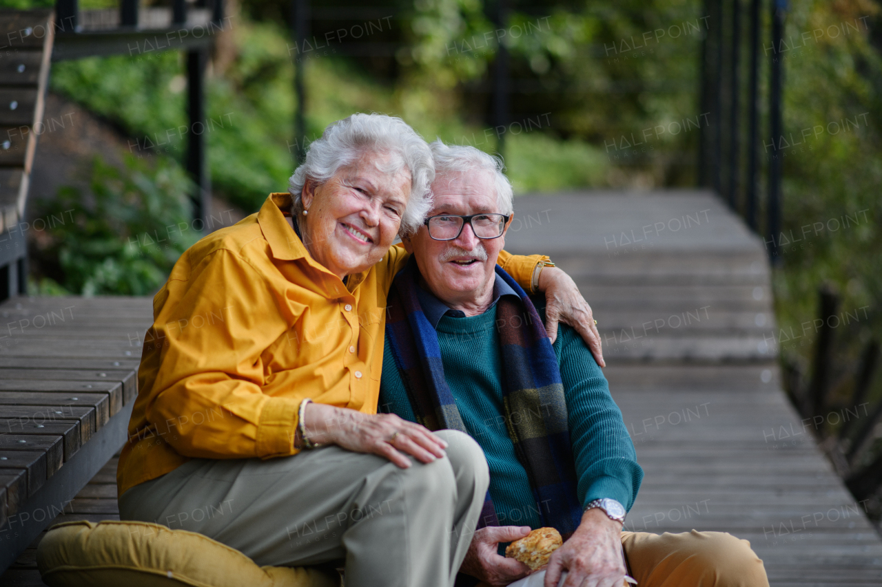 Happy senior couple resting near lake after autumn walk.