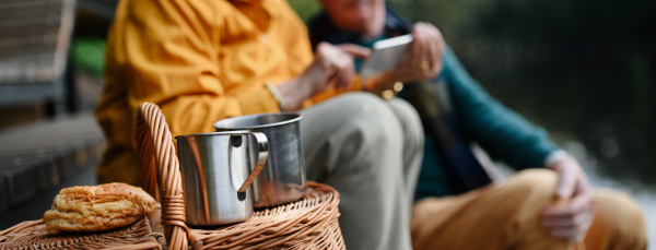 Mid section of senior couple resting near lake after walk and looking at a smartphone.