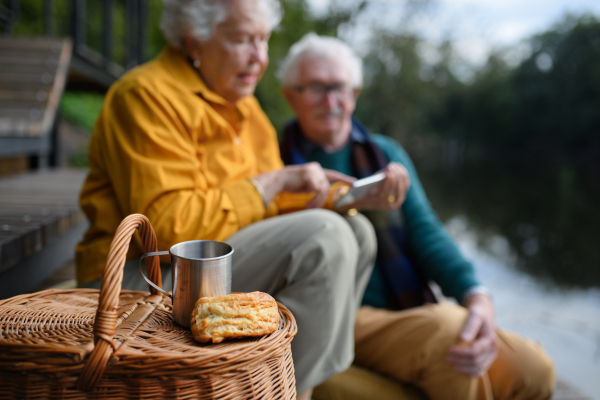 Happy senior couple having picnic and resting near lake after autumn walk.