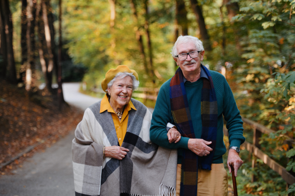 Happy senior couple in autumn clothes walking in park together.