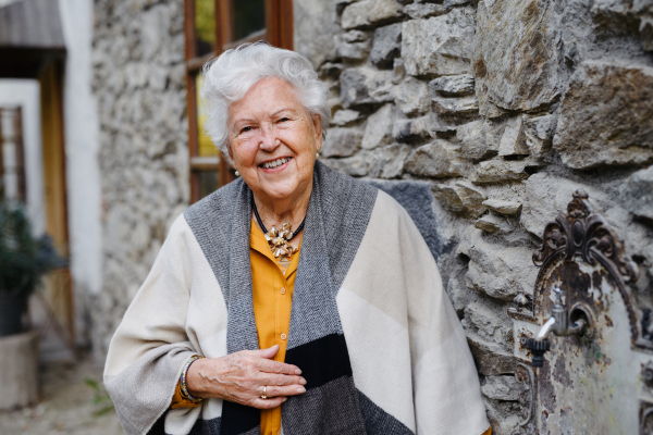 Portrait of elegant senior woman standying near to countryhouse. Image with copy space.