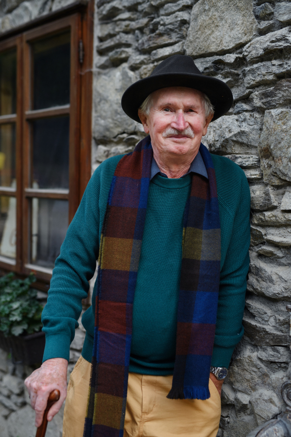 Portrait of senior man with black hat leaning of a house.