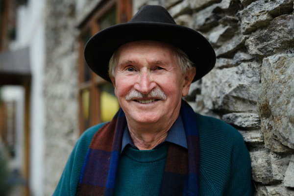 Portrait of senior man with black hat leaning of a house.