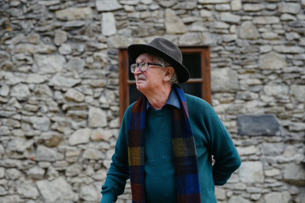 Portrait of senior man with black hat leaning of a house.