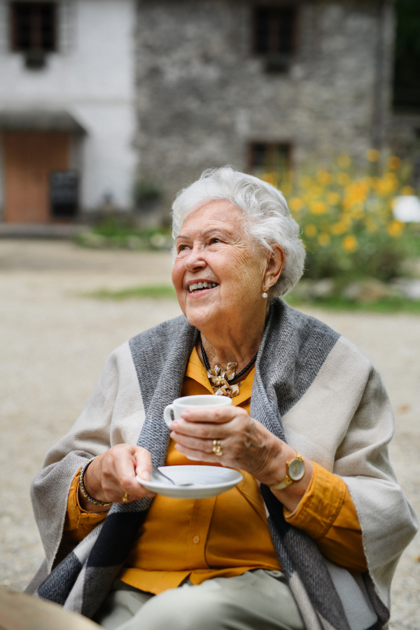 Portrait of senior woman enjoying cup of coffee outdoor in cafe. Beautiful elderly woman resting in backyard on warm autumn day.