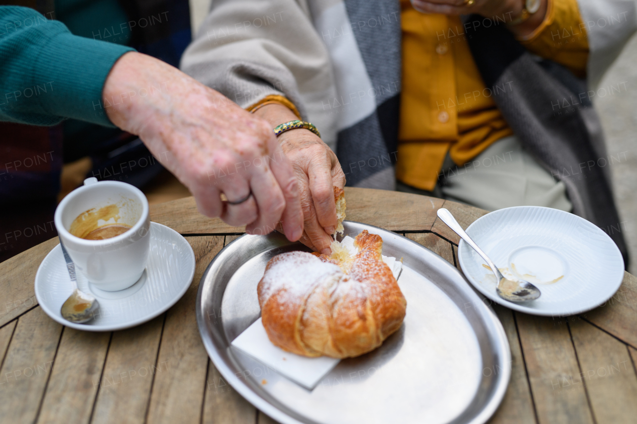 Close-up of senior couple enjoying cup of coffee and cake outdoor in a cafe.