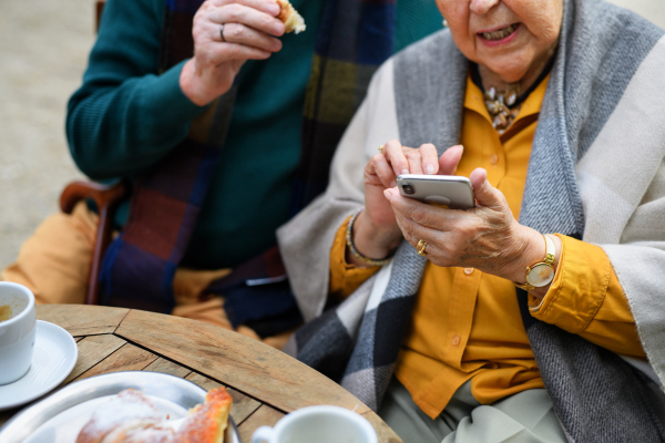 Close up of senior wife and husband looking at the photos on smartphone. Senior couple having coffee at outdoor coffee shop.