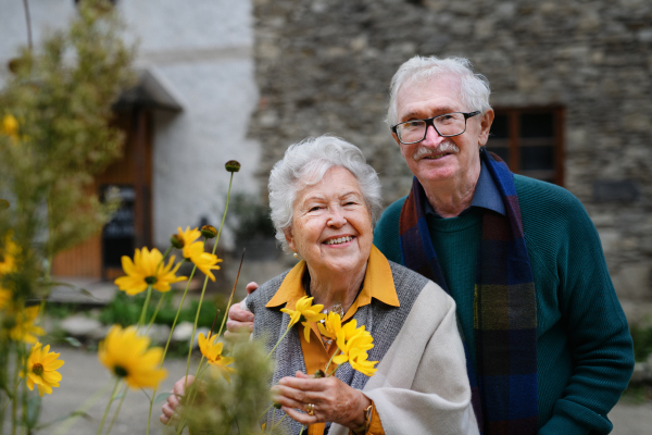 Happy senior couple at autumn city walk, posing with the flowers.