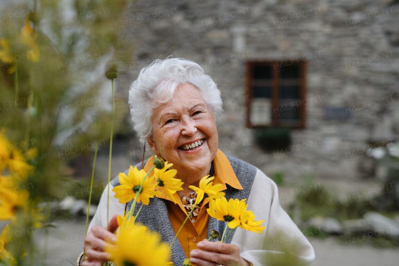 Portrait of happy senior woman, standing outdoor and posing with the flowers.