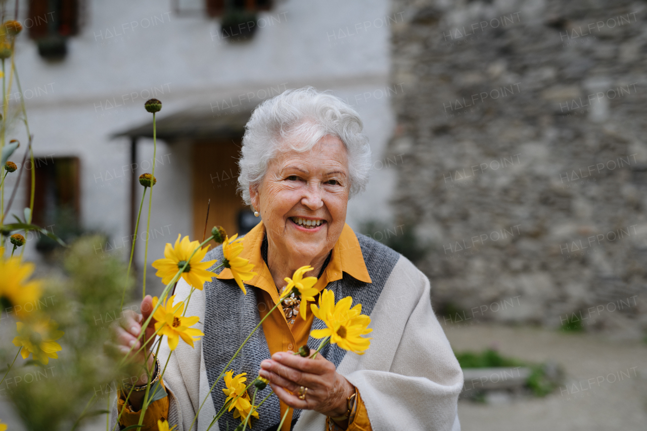 Portrait of happy senior woman, standing outdoor and posing with the flowers.